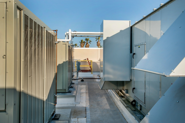 A ground-level perspective shows a row of large commercial air handling units and HVAC equipment installed on a flat industrial rooftop with palm trees visible in the distance.