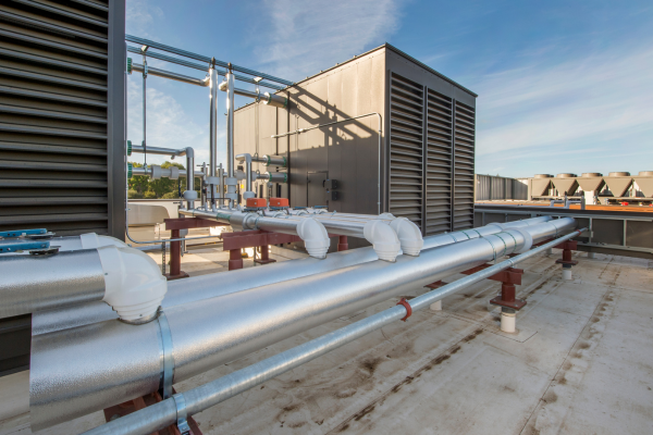 A wide-angle view shows large silver insulated HVAC pipes and high-capacity air handler units installed on a flat commercial rooftop under a blue sky.