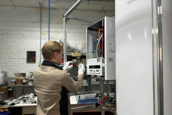 A technician wearing white gloves uses a screwdriver to make precise adjustments to the internal control panel of a modern wall-mounted furnace in a workshop environment.