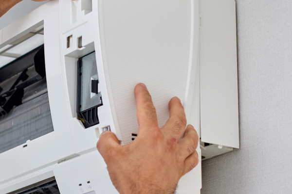 A close-up view of a technician's hands using a small screwdriver to carefully secure thin, multicolored thermostat wires into the terminal blocks of an indoor HVAC unit.