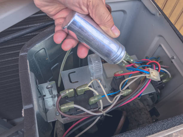 Close-up of an HVAC technician replacing or testing an air conditioner capacitor inside an outdoor AC unit during system maintenance or repair service.