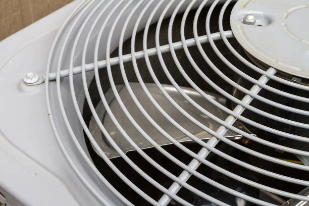 Close-up view of an outdoor HVAC condenser unit fan with a white protective grille, commonly used in residential air conditioning systems for cooling and airflow circulation.