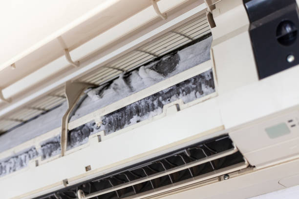 A close-up of an open wall-mounted indoor AC unit revealing heavily dust-covered and dirty evaporator coils and filters, indicating the unit is overdue for cleaning.