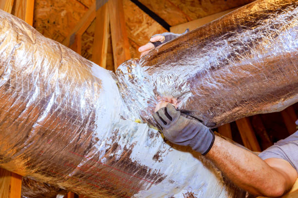 Gloved technician inspecting and handling an insulated flexible air duct connection in an attic