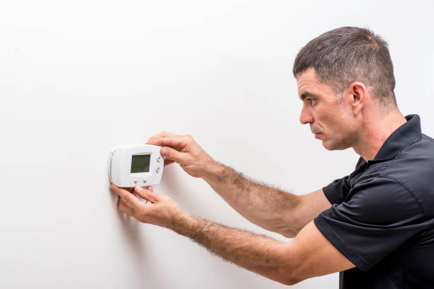 Technician mounting a digital thermostat on a white wall during installation