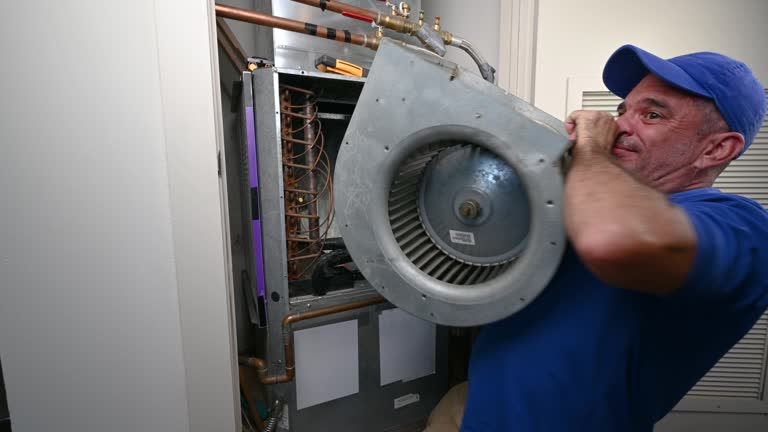 HVAC technician in a blue cap removing a blower fan assembly from an air handler unit for repair